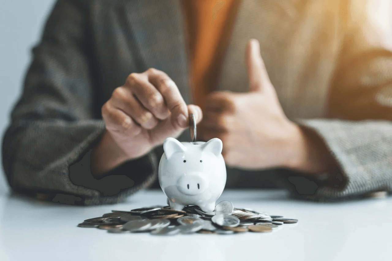 a businesswoman making thumb up hand sign while putting coin into piggy bank